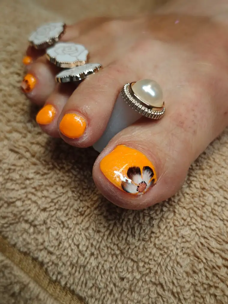 Pedicure med orange gelpolish og blomsterdesign på storetåen